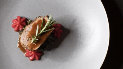 Gourmetgericht mit Fleisch, Sauce, Kräutern und rotem Gemüse auf grauem Teller