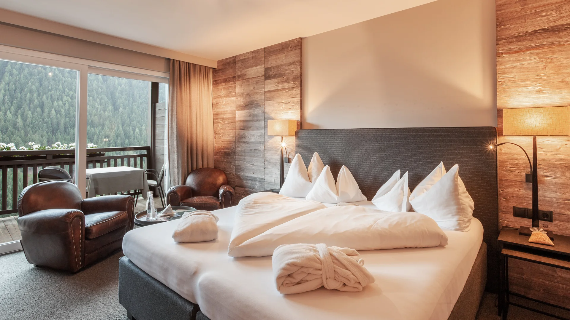 Gemütliches Hotelzimmer mit Bett, Ledersesseln und Bergblick vom Balkon
