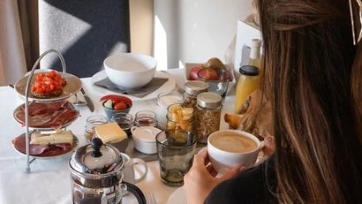 Frau sitzt am Tisch mit Frühstück und hält Kaffeetasse
