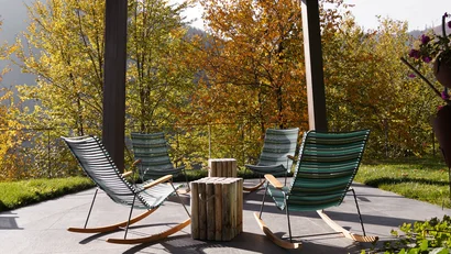 Vier Schaukelstühle in einem Garten mit herbstlich bunten Bäumen