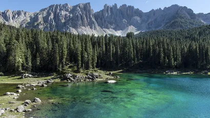 Türkisfarbener Bergsee vor Nadelwald und felsigen Gipfeln bei klarem Himmel