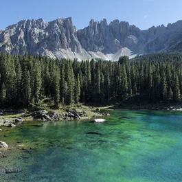 Türkisfarbener Bergsee vor Nadelwald und felsigen Gipfeln bei klarem Himmel