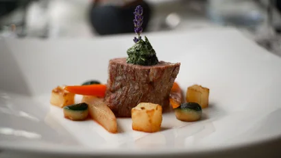 Gourmetgericht mit Steak, Sauce, Kartoffelwürfeln und Gemüse dekorativ auf Teller angerichtet