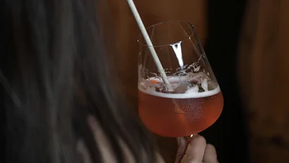 Frau hält ein Glas mit rosa Cocktail und Papierstrohhalm