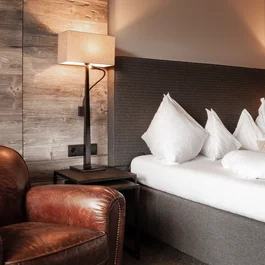 Beige Ledersessel neben einem Bett mit grauem Kopfteil und weißen Kissen