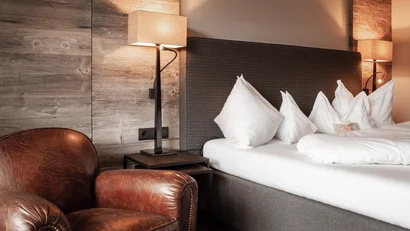 Beige Ledersessel neben einem Bett mit grauem Kopfteil und weißen Kissen