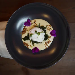 Elegantes Gericht mit pochiertem Ei, Sauce, Kräutern und Blüten auf schwarzem Teller