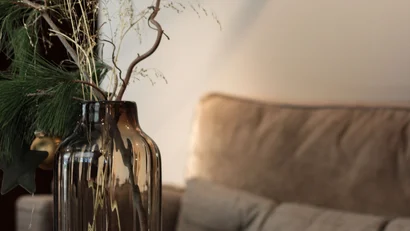 Braune Vase mit Zweigen und Kerzen auf Holztisch vor braunem Sofa