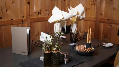 Restauranttisch mit Servietten, Brot, Kräutern und Menü vor Holzwänden