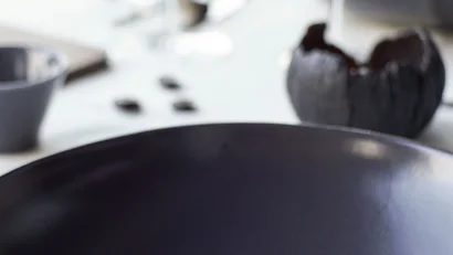 Fein angerichtete Jakobsmuscheln mit Gemüse und Blume auf schwarzem Teller