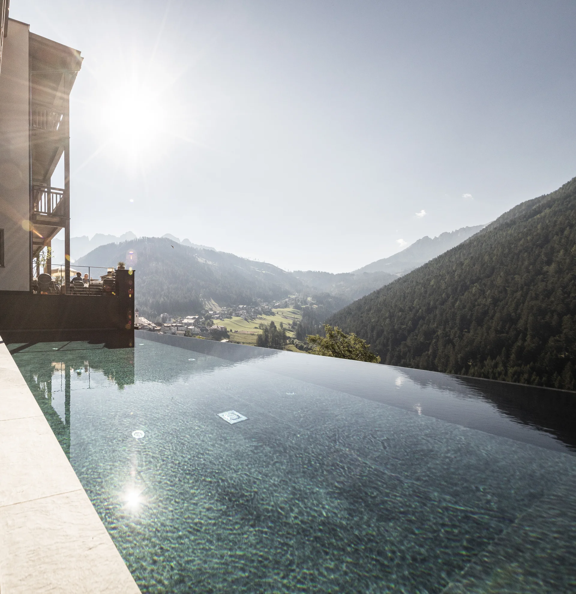 Infinity-Pool mit Bergblick und Reflexion an Glaswand bei sonnigem Wetter