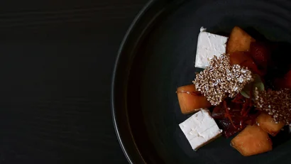 Kleines Gericht mit Käsewürfeln, Früchten und knusprigen Samen auf schwarzem Teller