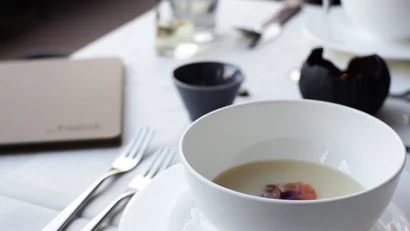 Weiße Schüssel mit cremiger Suppe und Garnitur auf gedecktem Tisch