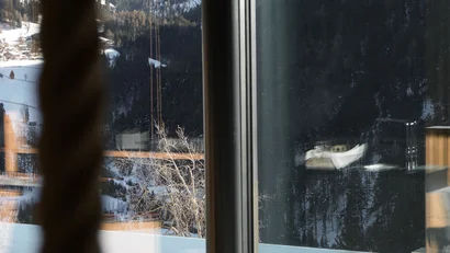 Blick durch ein Fenster auf verschneite Berge und einen Pool