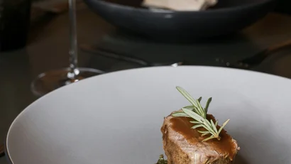 Elegantes Gericht mit Fleisch, grünen Blättern und roter Soße auf grauem Teller