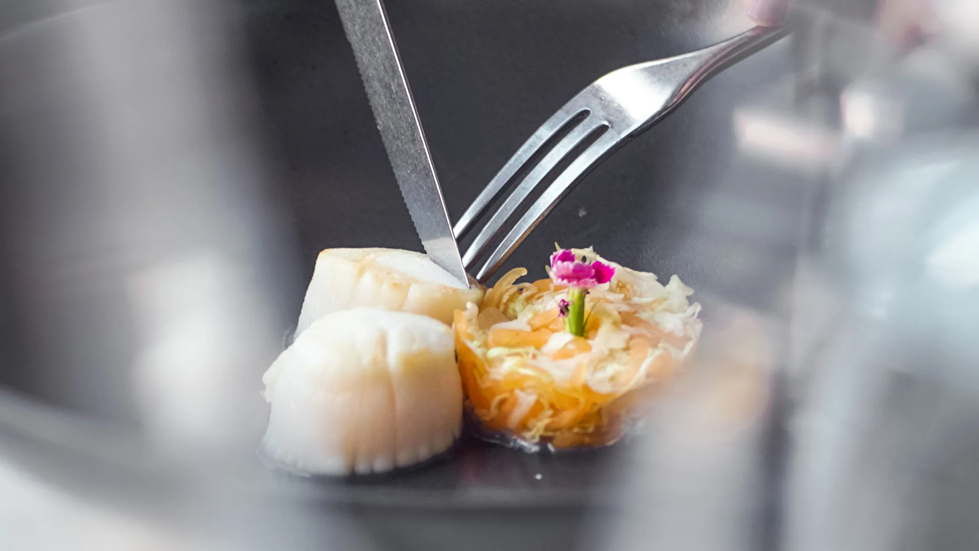 Person schneidet zartes Essen, zwei Jakobsmuscheln und ein dekoriertes Gericht