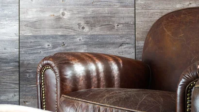 Nahaufnahme eines vintage braunen Ledersofas vor einer Wand aus grauen Holzdielen