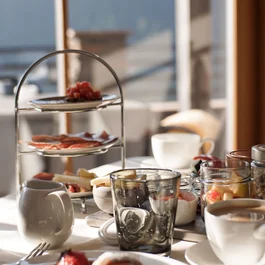 Frühstückstisch mit Croissant, Aufschnitt, Käse und Kaffee bei Sonnenlicht