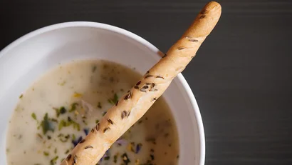 Schüssel mit cremiger Suppe und einem Kümmelstangenbrot darauf