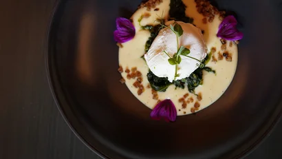 Poached Ei auf Spinat mit Sauce und essbaren Blüten auf dunklem Teller