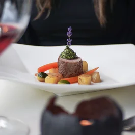 Fein angerichtetes Gericht mit Fleisch, Gemüse und einer Lavendelblüte auf weißem Teller