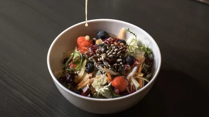 Person gießt Dressing über einen frischen Salat mit Beeren und Samen